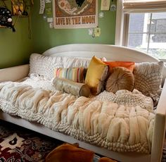 a day bed with pillows on top of it in front of a green wall and window