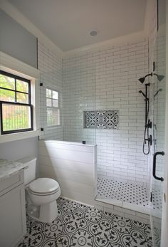 a white toilet sitting in a bathroom next to a walk in shower and sink under a window