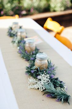 some jars are lined up on a table with lavenders and baby's breath