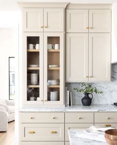 a kitchen with white cabinets and marble counter tops, gold pulls on the cupboards