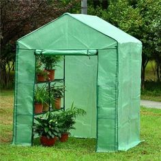 a green house with potted plants in it on the grass next to a tree