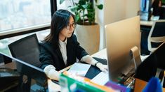 a woman sitting at a desk with a laptop computer in front of her and another person behind her