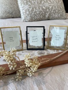 three small frames with writing on them sitting on a bed next to flowers and pillows