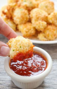 a person dipping some food into a small white bowl filled with tomato sauce and bread crumbs