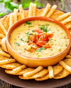 a bowl of dip surrounded by french fries on a plate with tomatoes and parsley