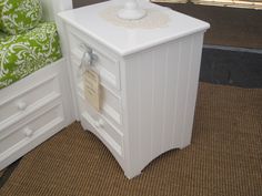 a white night stand sitting next to a green chair on top of a carpeted floor