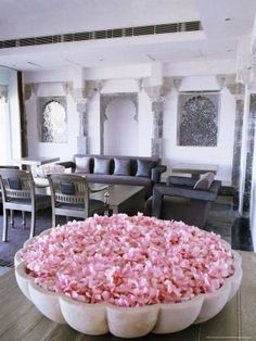 a large bowl filled with pink flowers sitting on top of a wooden table next to chairs