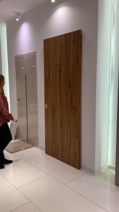 a woman standing in a bathroom next to a wooden door and white tile flooring