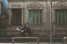 two people sitting on a bench in front of an old building with green shutters