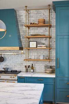 a kitchen with blue cabinets and marble counter tops, gold accents on the shelves and shelving