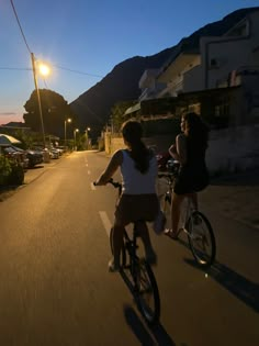 two women riding bikes down the street at night with their backs turned to the camera