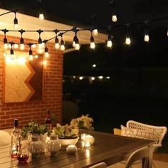 an outdoor dining area with lights strung from the ceiling and table set for two, surrounded by white wicker chairs