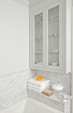 a bathroom with marble counter tops and white cabinets, along with glass shelves above the bathtub