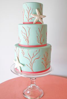 a three tiered cake decorated with seaweed and starfish on a pink table