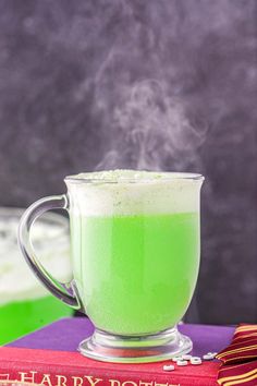 a green drink sitting on top of a book next to a cup filled with liquid