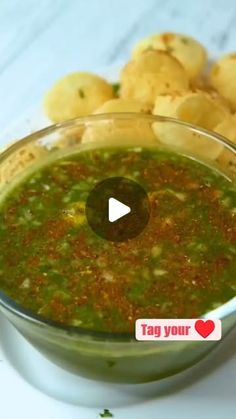 a bowl filled with green sauce next to crackers on a white tableclothed surface