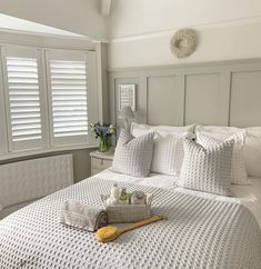 a bed with white sheets and pillows in a bedroom next to two window shutters