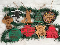 christmas ornaments are hanging from the branches on a white wooden background with green and red decorations