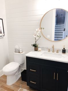 a white toilet sitting next to a bathroom sink under a round mirror on top of a wooden floor