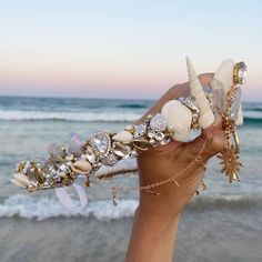 a hand holding up a bracelet with shells and seashells on it at the beach