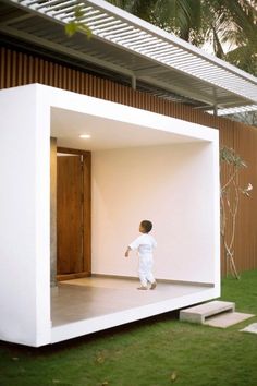 a little boy standing in the doorway of a white house with grass and steps leading up to it