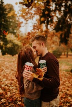 a man and woman kissing in the fall leaves with cups of coffee on their lap