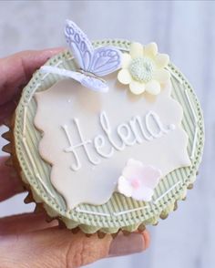 a hand holding a cupcake with the word hello on it and butterflies flying around