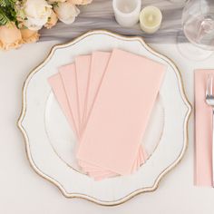 pink napkins are sitting on a white plate next to silverware and flowers in vases