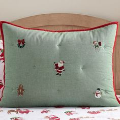 a green pillow with santa clause on it sitting on a bed next to a wooden headboard