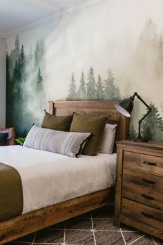 a bedroom with a bed, nightstand and painting on the wall behind it that has pine trees