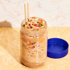 a jar filled with noodles and vegetables on top of a table next to a blue container