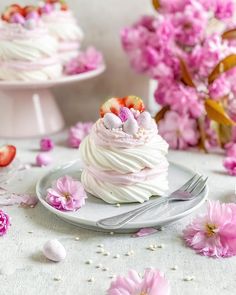 a white plate topped with a cupcake covered in frosting and strawberries next to pink flowers