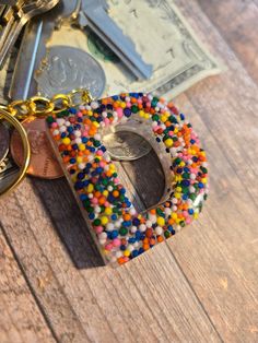 the letter d is made out of candy beads and sits on a wooden table next to money