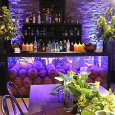 a bar with lots of bottles and plants on the table in front of purple brick walls