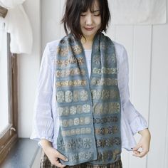 a woman standing next to a window wearing a blue and brown scarf with flowers on it