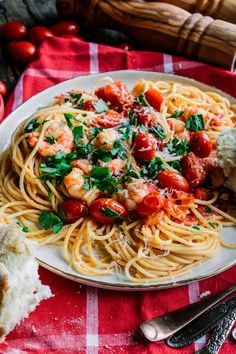 a plate of pasta with shrimp, tomatoes and parmesan cheese on a red checkered table cloth