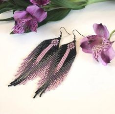 two pairs of black and pink beaded fringe earrings next to purple flowers on a white surface