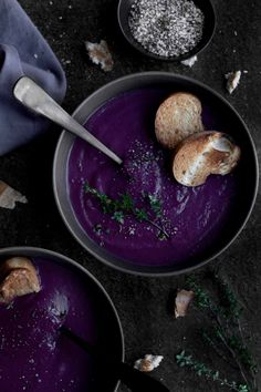 two bowls filled with purple soup on top of a black table next to silver spoons