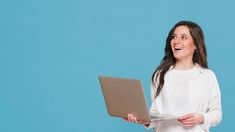 a woman holding a laptop computer and smiling at the camera while standing against a blue background