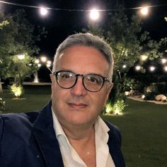 a man wearing glasses is standing in front of some trees and lights at night time