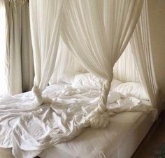 an unmade bed with white sheets and drapes