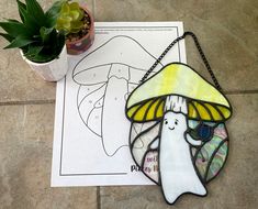 a stained glass piece with a mushroom on it next to a potted plant and coloring book