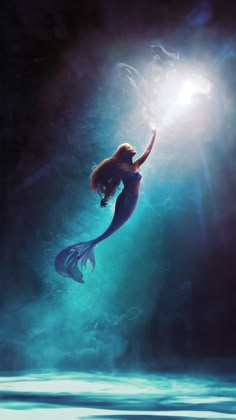 the little mermaid is floating in the water with her arms up to the light shining on her head