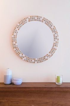 a round mirror sitting on top of a wooden shelf next to a vase and candle