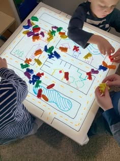 two children are playing with their toys on the floor in front of a white board