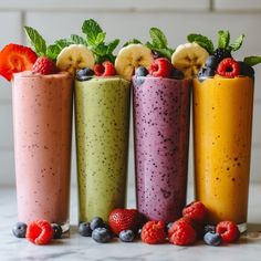 four smoothies are lined up with berries, bananas and strawberries