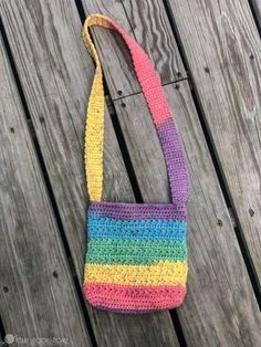 a multicolored crocheted purse sitting on top of a wooden table next to a fence