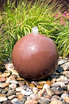 a large ball sitting on top of a pile of rocks next to some grass and flowers