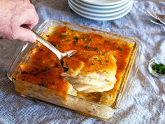 a person is cutting into some food in a glass casserole dish on a table