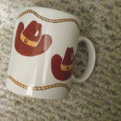 a white coffee cup with red and yellow cowboy hats on it's sides is sitting on the carpet